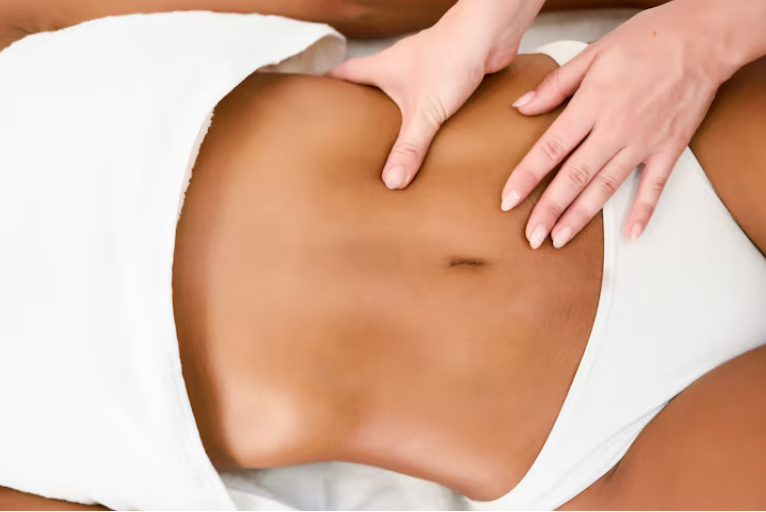 A therapist performs an abdominal massage on a client lying on a treatment bed covered with a towel.