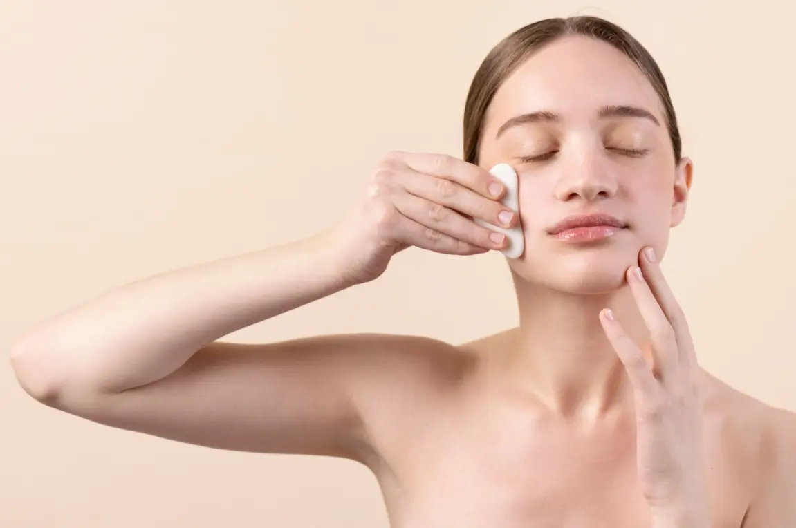 Woman gently cleansing her face with a cotton pad as part of a daily skincare routine.