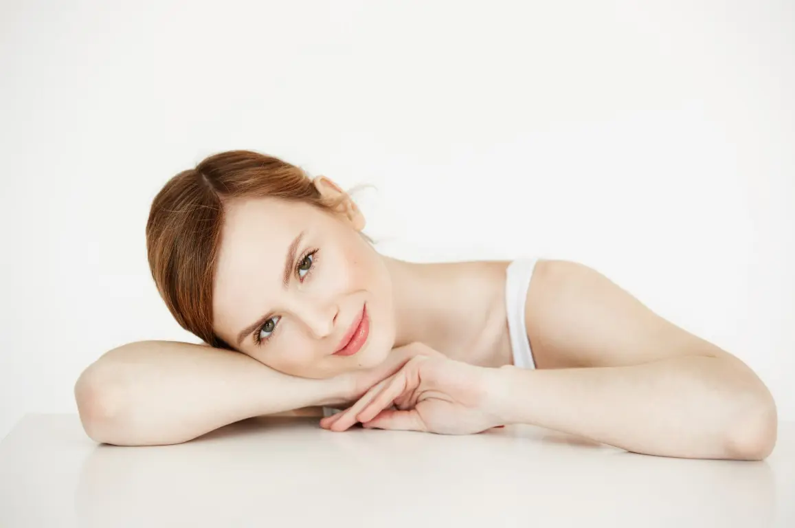 Woman with clear, radiant skin resting her head on her arms, showcasing a healthy and refreshed complexion.